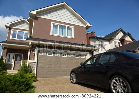 Car near the garage of new two-storied brown cottage with white roof