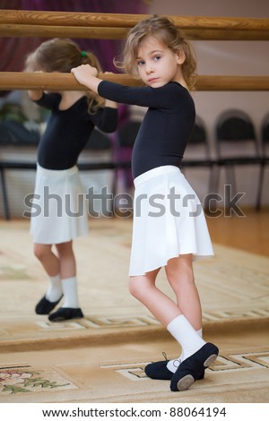 Little girl poses at ballet barre. Reflection in mirror.