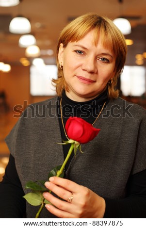 Smiling middleaged woman with red rose in hands stand in empty cafe