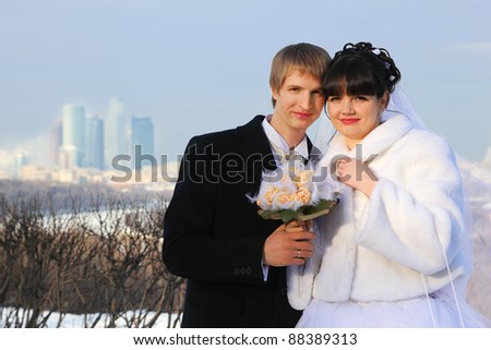smiling groom and bride holding bouquet of roses and look at camera at winter outdoors