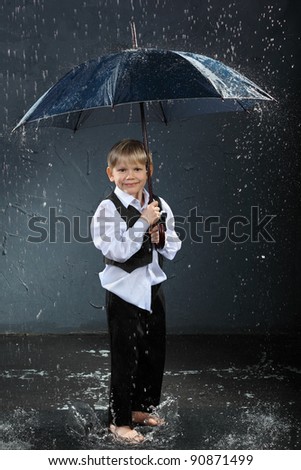 smiling boy dressed in white shirt standing under umbrella in rain