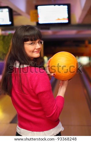 happy girl with yellow ball stands back to camera in bowling club and preparing to throw