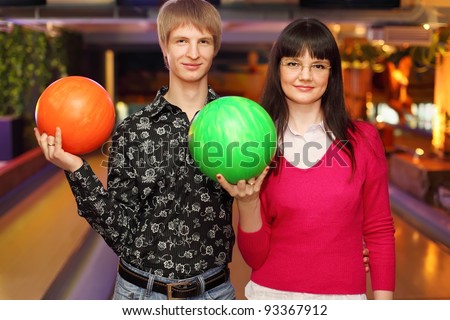 happy wife and husband with balls stand in bowling club and look at camera