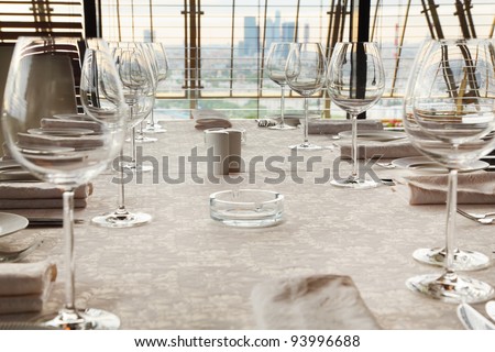 glasses at table with white tablecloth in restaurant; skyscrapers outside window
