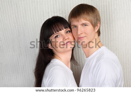 Young happy man and woman dressed in white shirts on white knitted background