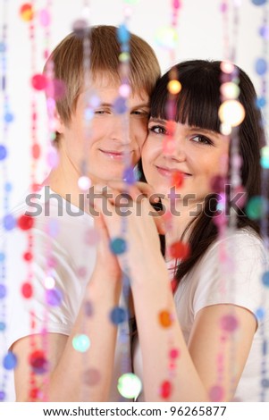 Young man and woman dressed in white shirts hold hands behind transparent curtain of beads; focus on pair