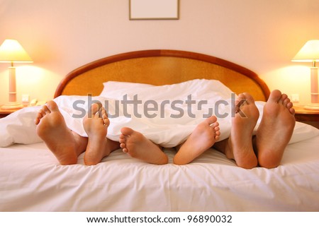 Mother, father and child lie on soft big bed with white sheets; focus on feet