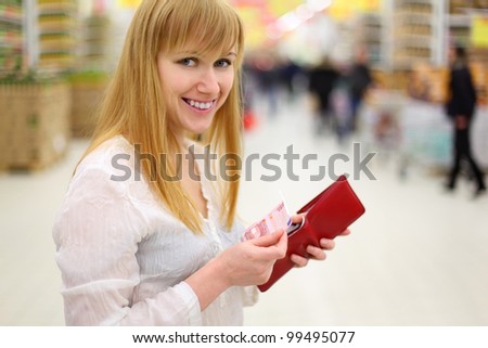 Happy girl gets money from her red purse in store and looks at camera; shallow depth of field