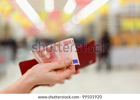Woman hands gets money from her red purse in store; shallow depth of field