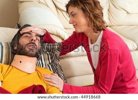 A beautiful young couple. The wife is patting her husband on the head. He is in a neck brace and appears to be in pain or drowsy.