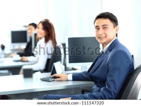 Portrait of a smiling young businessman working on computer at office with his colleagues