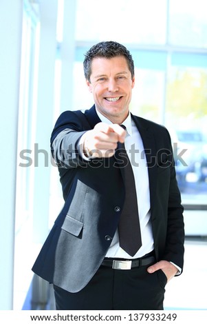Portrait of smiling mature business man pointing at you in office