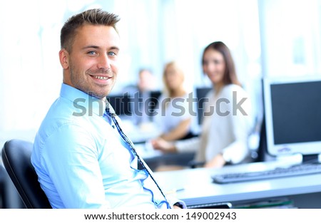 Portrait of young businessman in office with colleagues in the background