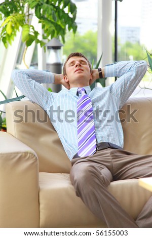 Young relaxed business man with hands behind head at work