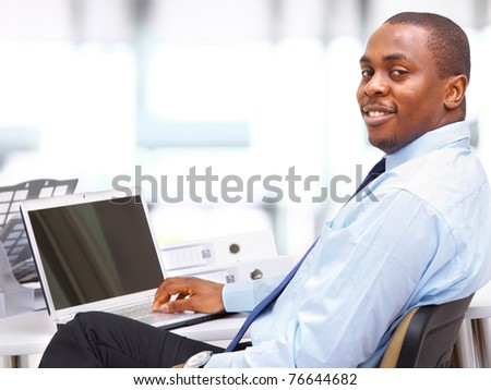 Portrait of a happy African American entrepreneur displaying computer laptop on light background