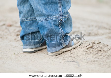Closeup on a kids feet wearing grey sandals and jeans over ground