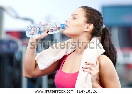 Young oman drinking water after sports. Fitness gym.