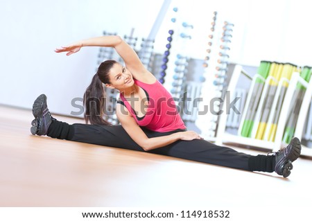 Young fitness woman doing stretching exercises on the floor at the sport gym club