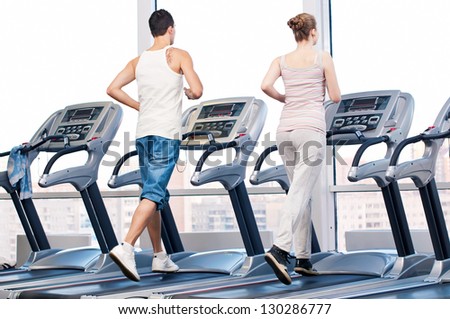 Young woman and man at the gym exercising. Run on a machine.