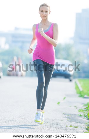 Jogging woman running in city park in sunshine on beautiful summer day. Sport fitness model caucasian ethnicity training outdoor for marathon.