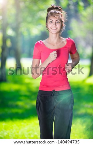 Young woman running outdoors in green park at lovely sunny summer day. Jogging