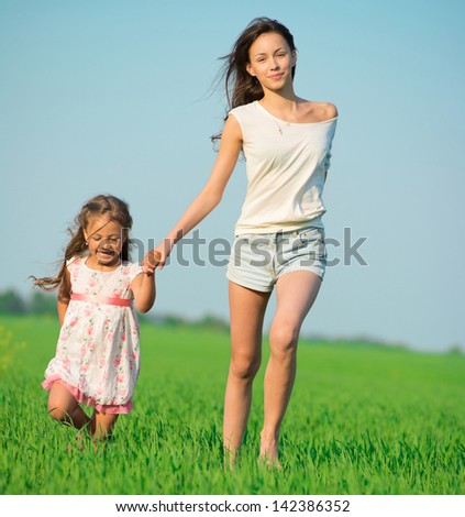 Young happy girls running down green wheat field with her friend together