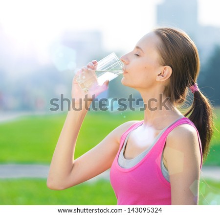 Portrait of young beautiful dark-haired woman wearing pink t-shirt drinking water after sport exercise at summer green park