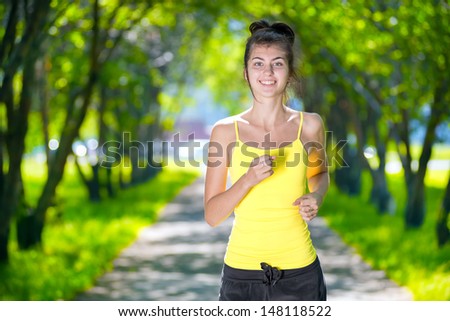 Young woman running outdoors in green park at lovely sunny summer day. Jogging