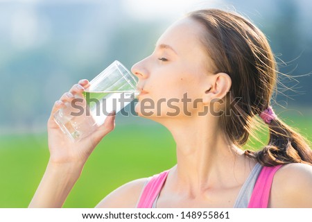 Portrait of young beautiful dark-haired woman wearing pink t-shirt drinking water after sport exercise at summer green park