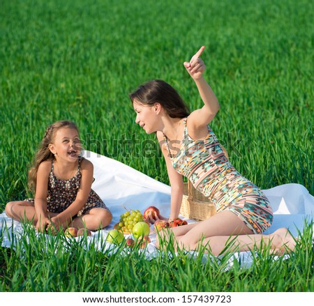 Happy girls on green grass at spring or summer park picnic. One girl point upside