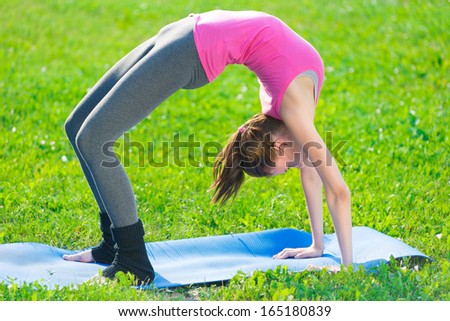 Beautiful sport woman doing stretching fitness exercise in city park at green grass. Yoga postures