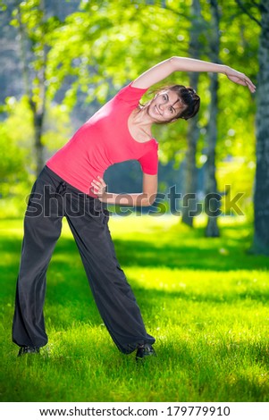Stretching woman in outdoor sport exercise. Smiling happy doing yoga stretches after running. Fitness model outside in park at summer day.