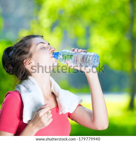 Young woman drinking cold mineral water after sport fitness exercise at green summer park