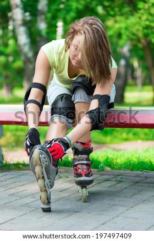 Woman skating in park. Girl going rollerblading sitting on bench  putting on inline skates. Sporty caucasian woman in outdoor fitness activities.