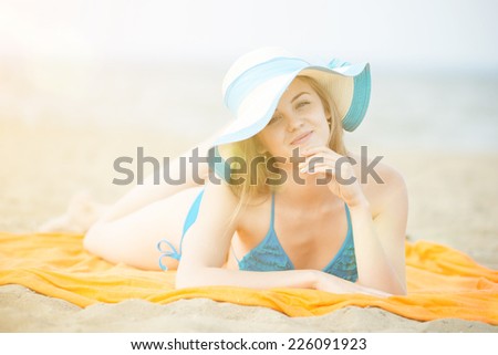 Young lady sunbathing on a beach. Beautiful woman posing at the summer sand beach. Outdoor summer portrait of pretty sport style woman in blue bikini. Ocean sea coast.
