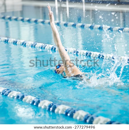 Young woman in goggles and cap swimming front crawl stroke style in the blue water indoor race pool