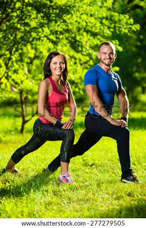 Man and woman doing stretching exercises at summer park.  Young couple exercising and stretching muscles before sport activity - outdoor in nature