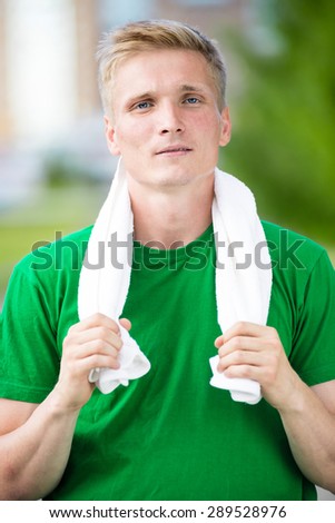 Tired man with white towel after fitness time and exercising in city street park at beautiful summer day. Sporty model caucasian ethnicity training outdoor.