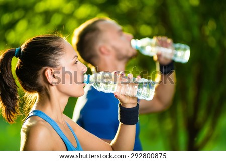 Man and woman drinking water from bottle after fitness sport exercise. Smiling couple with bottles of cold drink outdoors