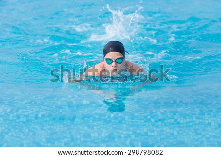 Young girl in goggles and cap swimming butterfly stroke style in the blue water pool