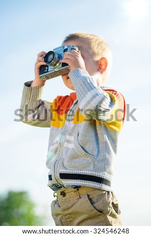 Little boy with an old camera shooting outdoor. Kid taking a photo using a vintage retro film cam. Green summer field.