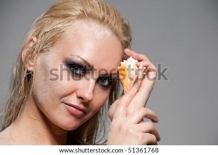 Close up portrait of blond woman with smoky eyes makeup, sand and shell