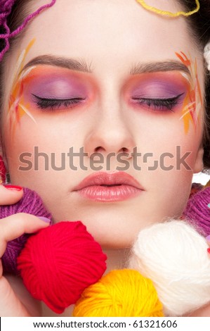 Closeup portrait of beautiful fashion woman with color face art. All in knitting style. Wool balls. Beads