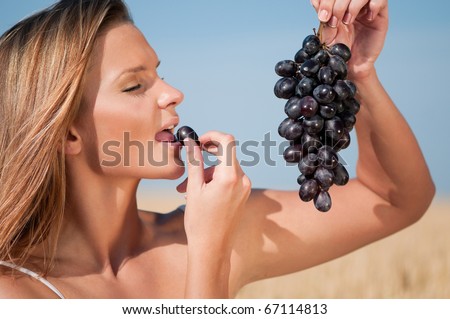 Beautiful woman with perfect hair and skin posing in wheat field and eating grapes. Summer picnic.