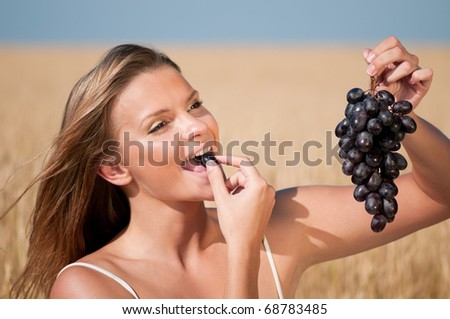 Beautiful woman with perfect hair and skin posing in wheat field and eating grapes. Summer picnic.