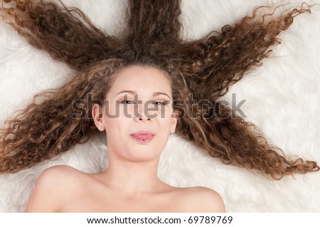 Closeup portrait of young emotional beautiful girl with perfect curly hair. Lying on white fur bed