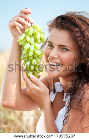 Beautiful woman with perfect hair and skin posing in wheat field and eating green grapes. Picnic.