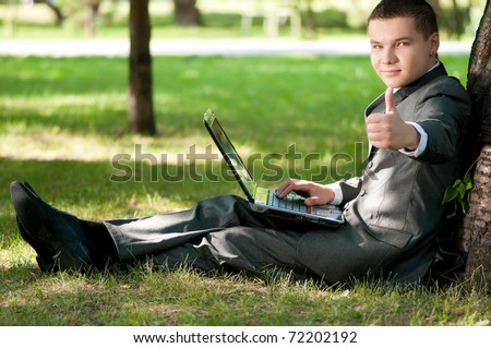 Young business man working on notebook laptop computer, at green park. Student. Thumbs up!