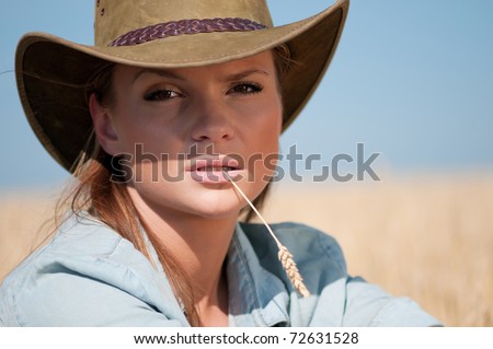 Beautiful cowboy woman with perfect hair and skin posing in country wheat field