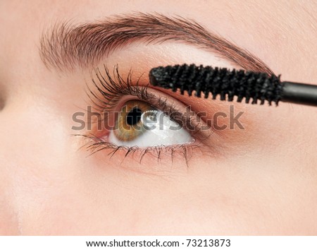 Beautiful young adult woman applying cosmetic mascara brush - close-up portrait of eyes zone
